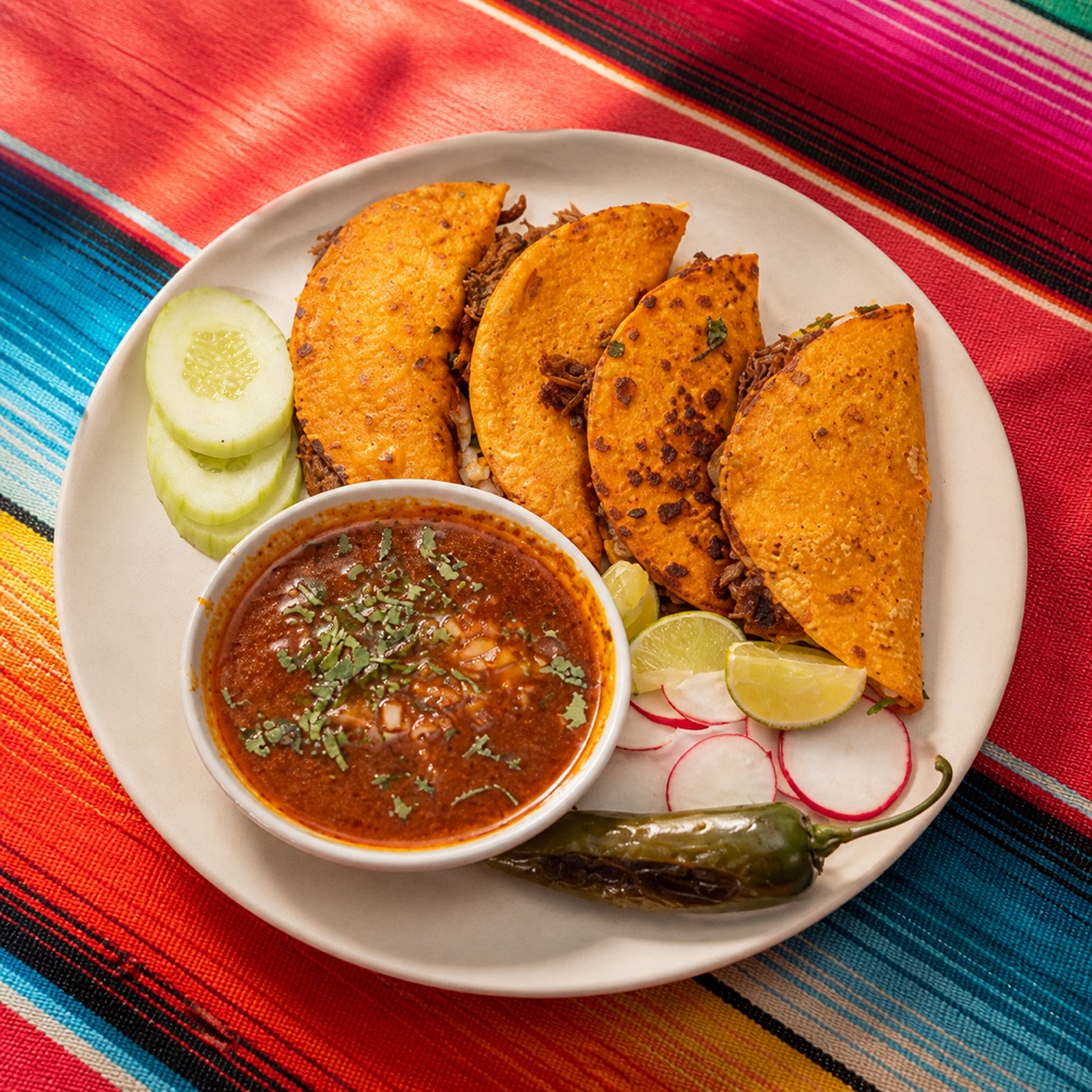 Birria tacos with consommé on a Mexican woven tablecloth